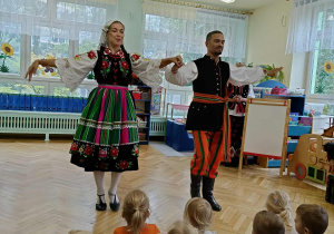 tancerze prezentują tańce ludowe, dzieci siedzą w sali przyglądając się ich tanecznym popisom