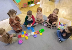 dzieci siedzą na dywanie budując drzewo z klocków