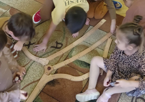 dzieci siedzą na dywanie budując drzewo z klocków
