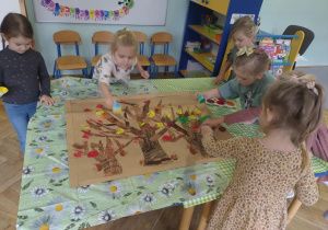 Dzieci stempluja liście na wcześniej wykonanych przez nich drzewach przy pomocy gąbki i farb.