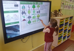 dziewczynka stoi przy tablicy multimedialnej wykonując zadanie