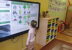 dziewczynka stoi przy tablicy multimedialnej wykonując zadanie