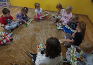 Dzieci siedzą na dywanie i oglądają ilustrowana instrukcje jak krok po kroku wykonać pierwsza pomoc