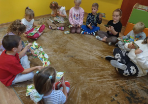 Dzieci siedzą na dywanie i oglądają ilustrowana instrukcje jak krok po kroku wykonać pierwsza pomoc