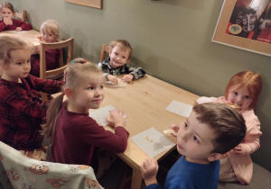 Dzieci siedzą przy stołach i delektują się słodkim ciasteczkiem.