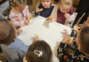 Dzieci siedzą przy stołach i delektują się słodkim ciasteczkiem.