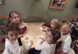 Dzieci siedzą przy stołach i delektują się słodkim ciasteczkiem.