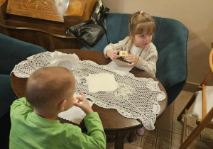 Dzieci siedzą przy stołach i delektują się słodkim ciasteczkiem.