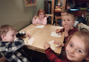 Dzieci siedzą przy stołach i delektują się słodkim ciasteczkiem.