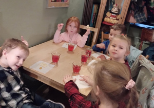 Dzieci siedzą przy stołach i delektują się słodkim ciasteczkiem.