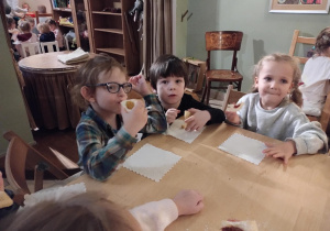 Dzieci siedzą przy stołach i delektują się słodkim ciasteczkiem.