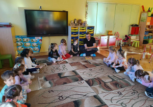 Pan Artur czyta książkę, dzieci siedzą w kole na dywanie słuchając opowieści