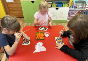 dzieci wyklejają pomarańczową bibułą dynię