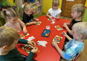 dzieci wyklejają pomarańczową bibułą dynię