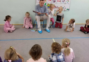 Dzieci siedzą w kole na dywanie, tata Zosi czyta książkę.