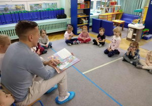 Dzieci siedzą w kole na dywanie, tata Zosi czyta książkę.
