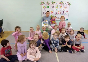 Dzieci wraz z tatą Zosi siedzą na dywanie pozując do grupowego pamiątkowego zdjęcia z głównego czytania.