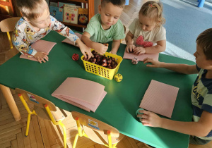 Dzieci przy stoliku liczą kasztany i rzucają kostką.