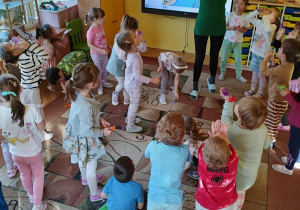 dzieci stoją na dywanie, dmuchają w piórka