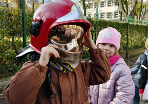 Dzieci przymierzają kaski strażackie.