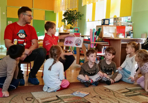 dzieci siedzą w kole na dywanie, Bartek czyta książkę pokazując ilustrację