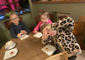 dzieci siedzą przy stolikach na których znajduje się poczęstunek