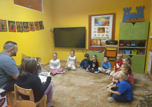 dzieci siedzą na dywanie słuchając czytanej książki przez tatę Michaliny